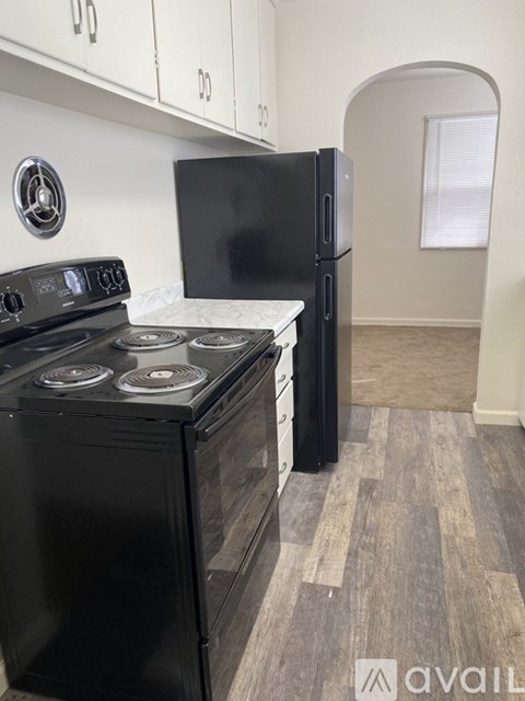 A black stove top oven with four burners and a black refrigerator in a kitchen.