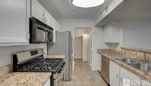 A kitchen with a black microwave above a stove and a refrigerator to the right.
