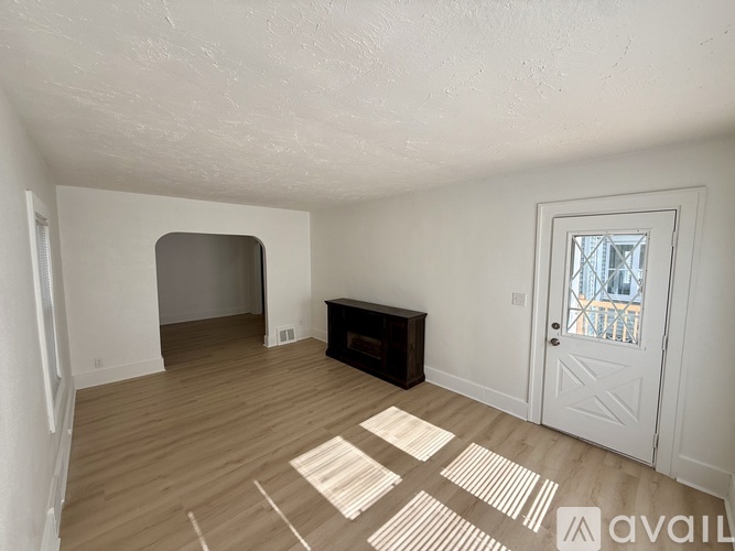 A room with a white door, a window, and a wooden floor.