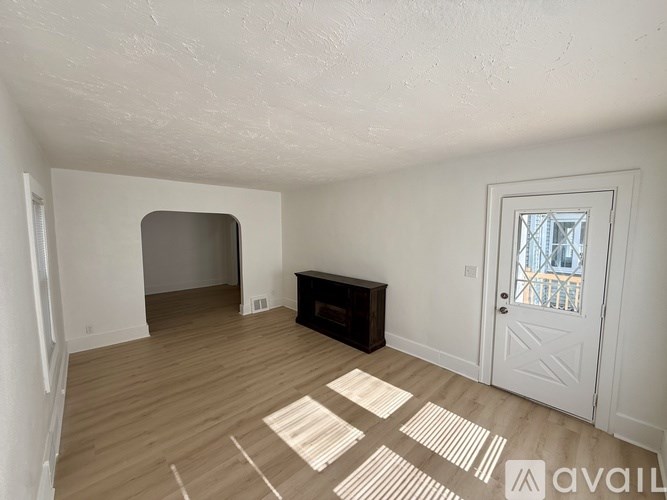 A room with a white door, a window, and a wooden floor.