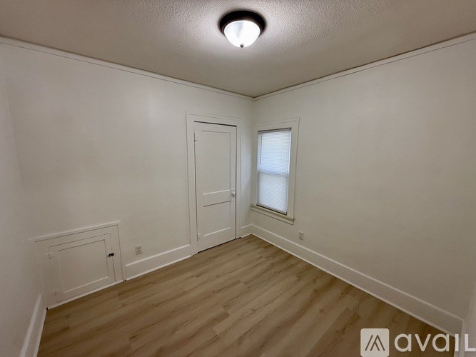 A room with a wooden floor and white walls, featuring a door and a window.