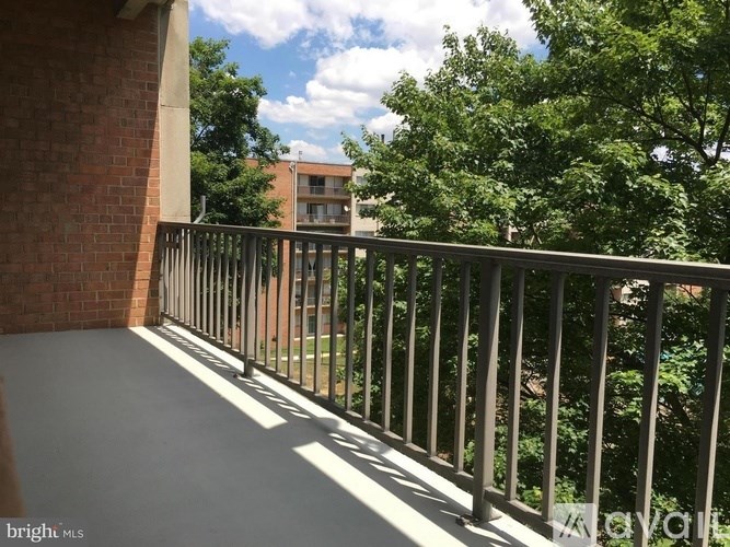 A balcony with a metal railing and a view of a brick building and trees.