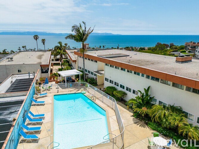 A swimming pool with lounge chairs and a view of the ocean.