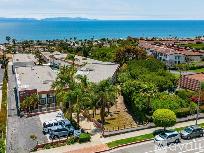 A parking lot with cars and a building in the foreground with a view of the ocean in the background.
