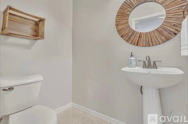 A bathroom with a white tub and sink, a round mirror, and a wooden picture frame on the wall.