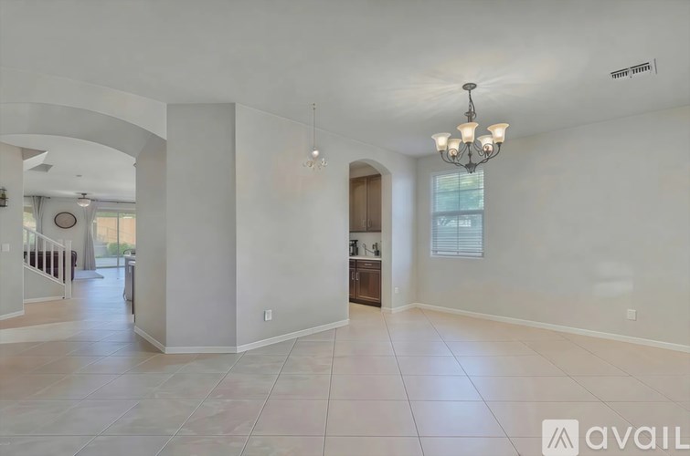 A spacious living room with a chandelier and a kitchen in the background.