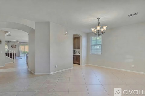A spacious living room with a chandelier and a kitchen in the background.
