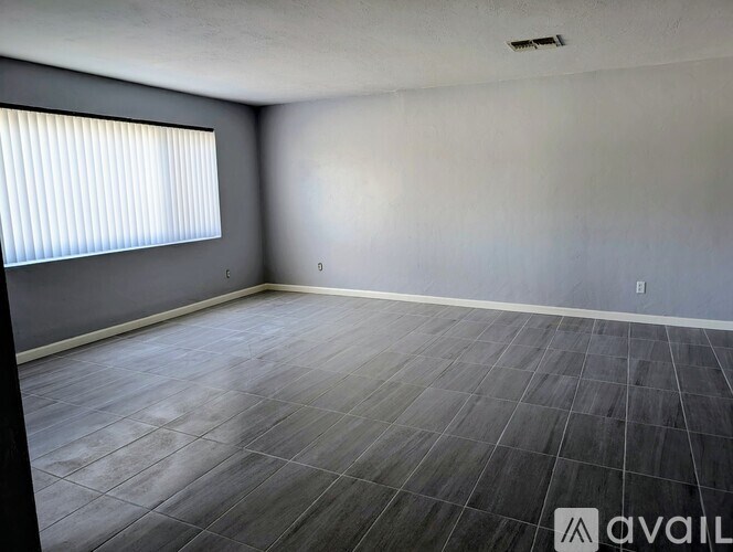 A room with a grey floor and a window with blinds.