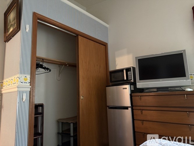 A small room with a fridge, microwave, and a TV on top of a dresser.
