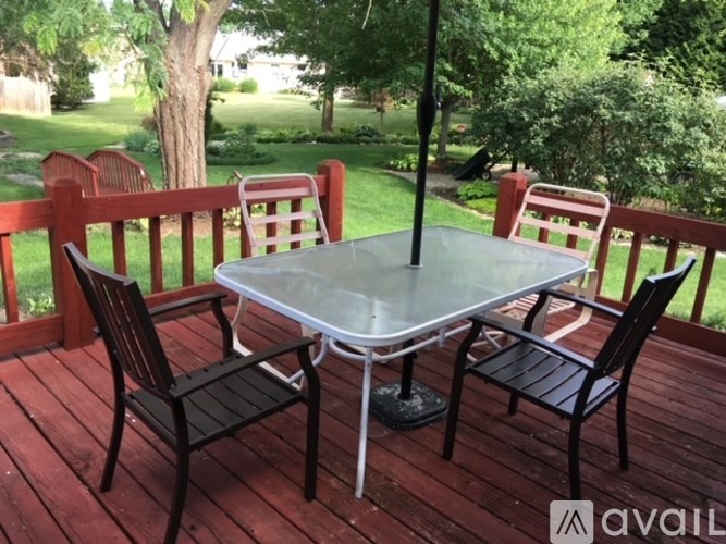A glass table with four chairs is on a wooden deck.