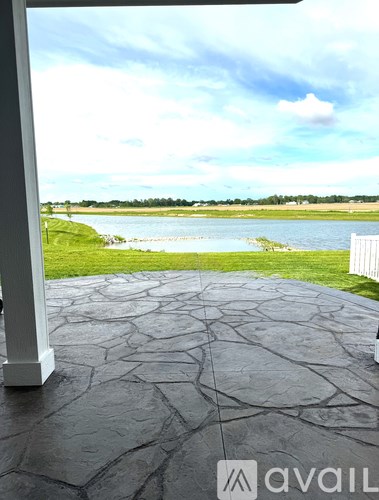 A patio with a stone floor leads to a grassy area with a lake and trees in the distance.