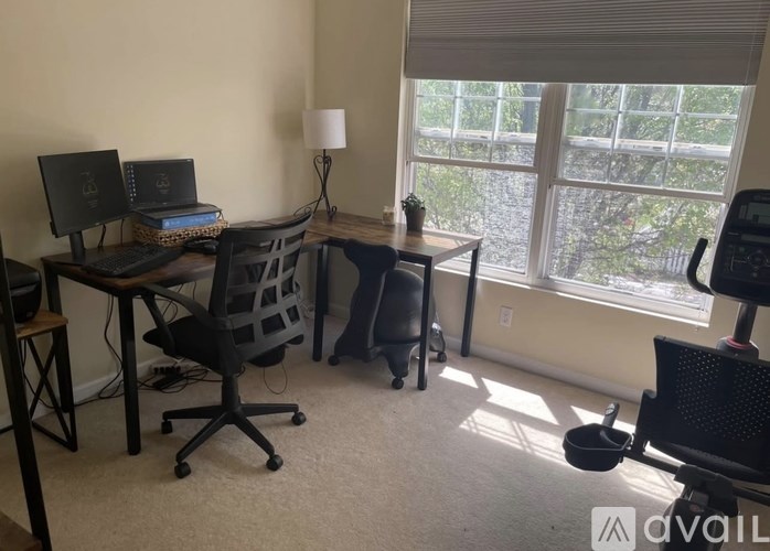 A room with two desks and chairs, one of which has a laptop on it.