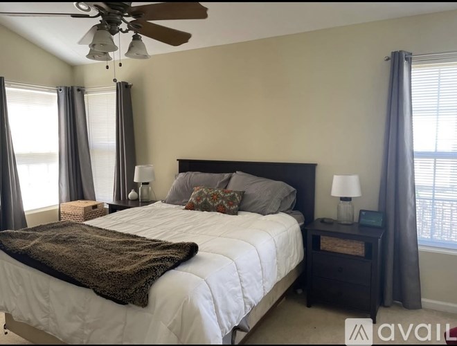 A bedroom with a large bed, a ceiling fan, and a window with curtains.