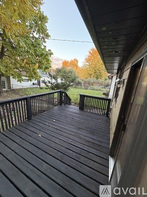A wooden deck with a railing and a view of a tree with yellow leaves.