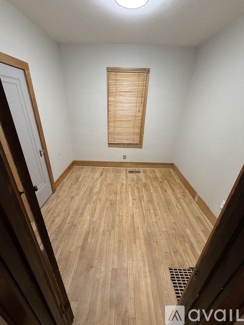 A room with wooden flooring and a window with blinds.
