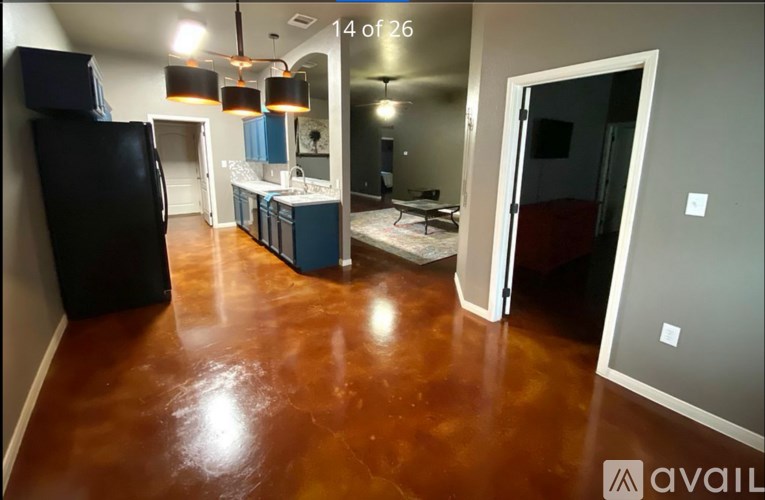 A kitchen area with a black fridge and brown flooring.