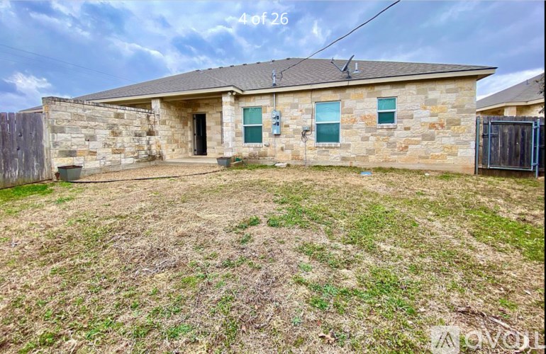 A house with a stone exterior and a brown roof is surrounded by a grassy area.