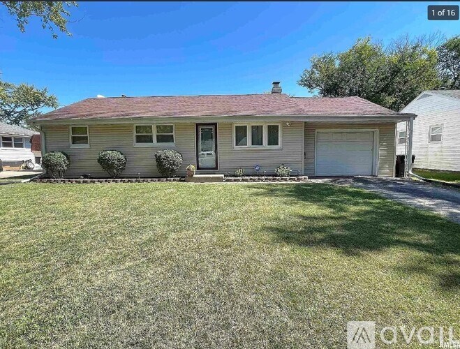 A house with a red roof and a white garage door is surrounded by a grassy lawn.