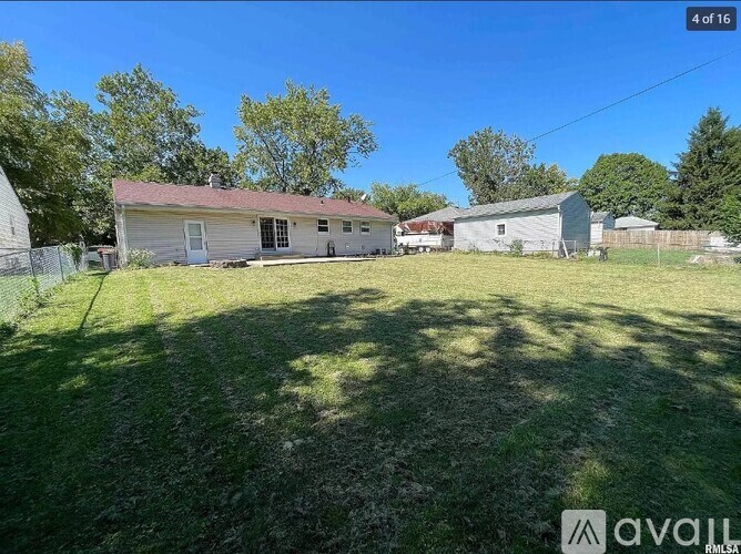 A grassy field with a house and a shed in the background.