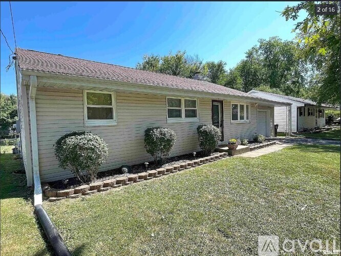 A house with a red roof and a white wall is surrounded by a grassy area and a few bushes.