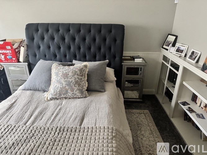 A bed with a black headboard and grey bedspread with a pillow on it.