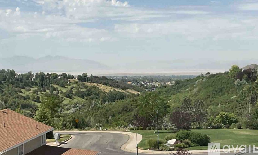 A house with a red roof is in the foreground of a landscape with a winding road and greenery.