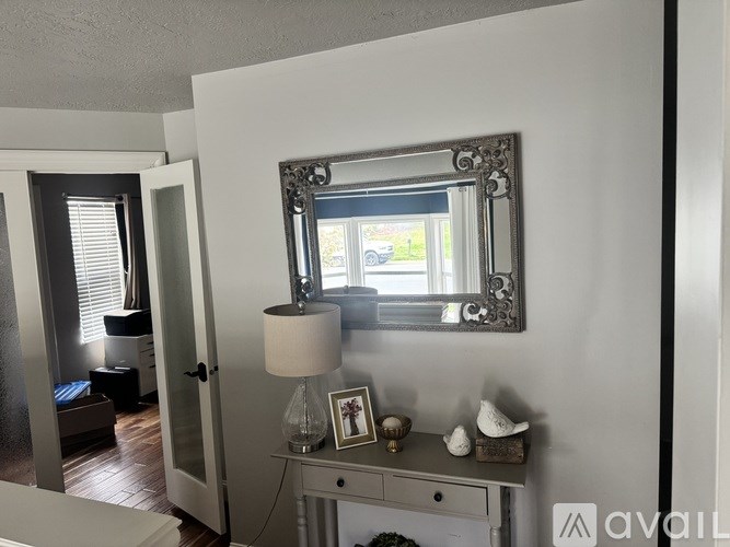 A mirror with a frame is on a dresser with a lamp and a picture frame.