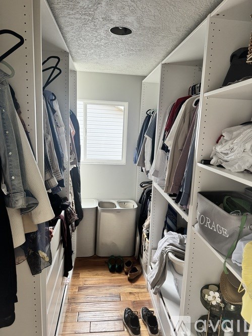 A small walk in closet with clothes on shelves and hanging on a rail.