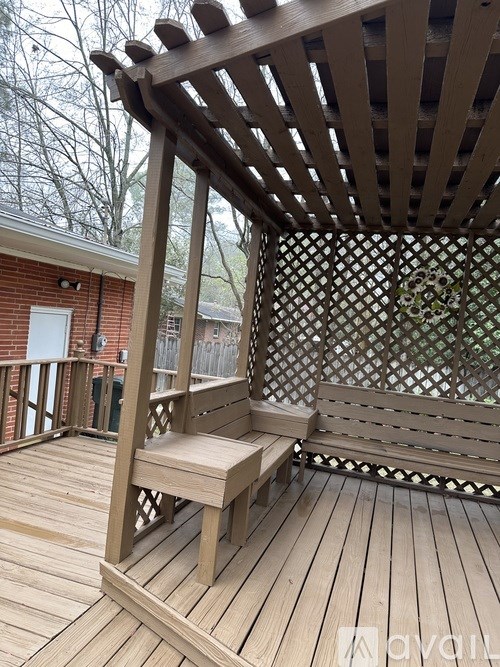 A wooden bench under a wooden pergola on a wooden deck.