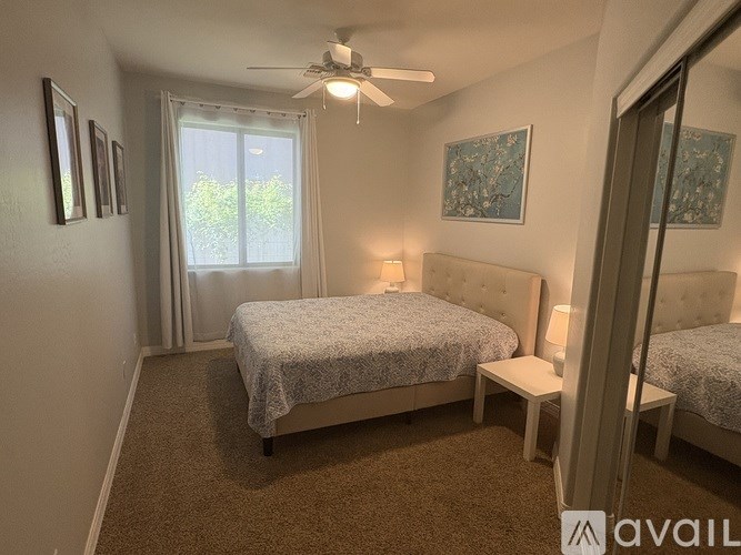 A bedroom with a bed, a window with curtains, a carpet, a ceiling fan, and a painting on the wall.