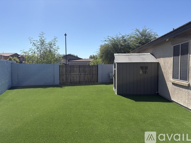 A backyard with a fence, a small shed, and a green lawn.