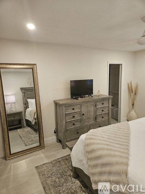 A bedroom with a large bed, a dresser with a mirror, and a television.