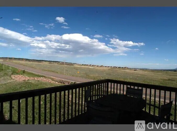 A balcony with a table and chairs overlooks a grassy field.