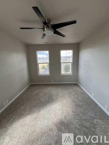 A room with a ceiling fan and two windows.