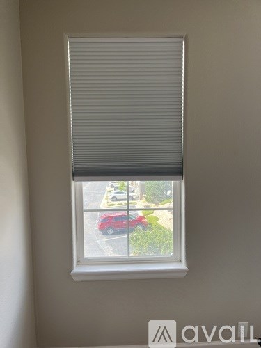 A window with blinds overlooking a street with cars and houses.