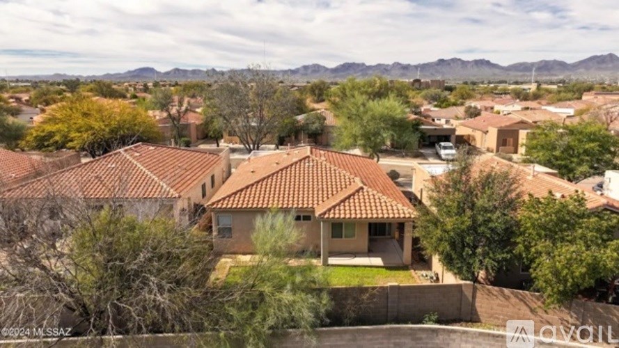 A house with a red tiled roof is surrounded by trees and mountains.