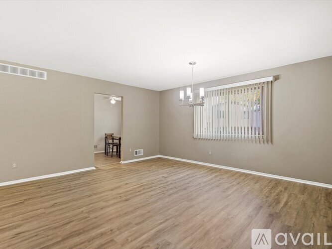 A spacious room with wooden flooring and a window with blinds.