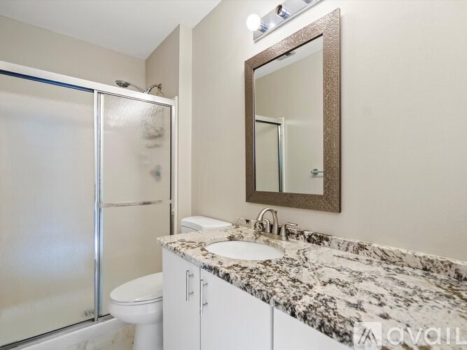A bathroom with a marble countertop, a toilet, a sink, and a mirror.