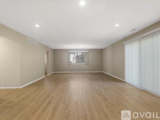 A spacious room with wooden flooring and a window with blinds.