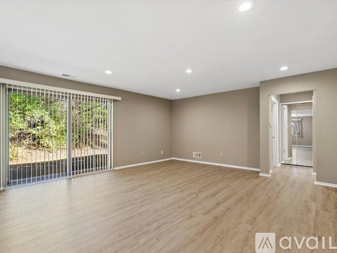 A spacious room with wooden flooring and a sliding glass door leading to a garden.