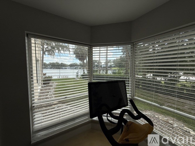 A room with a computer desk and a window with blinds overlooking a field.
