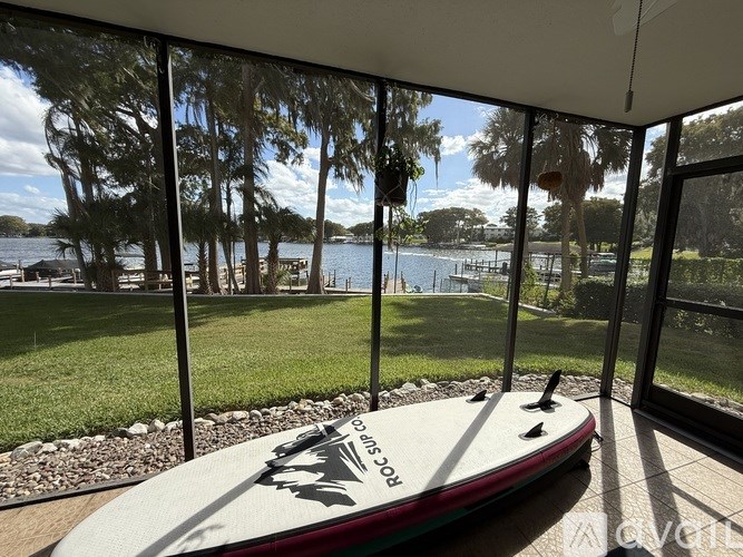 A surfboard is leaning against a glass wall with a view of a lake and trees.