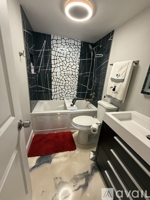 A bathroom with a white toilet, a red rug, and a black and white shower.