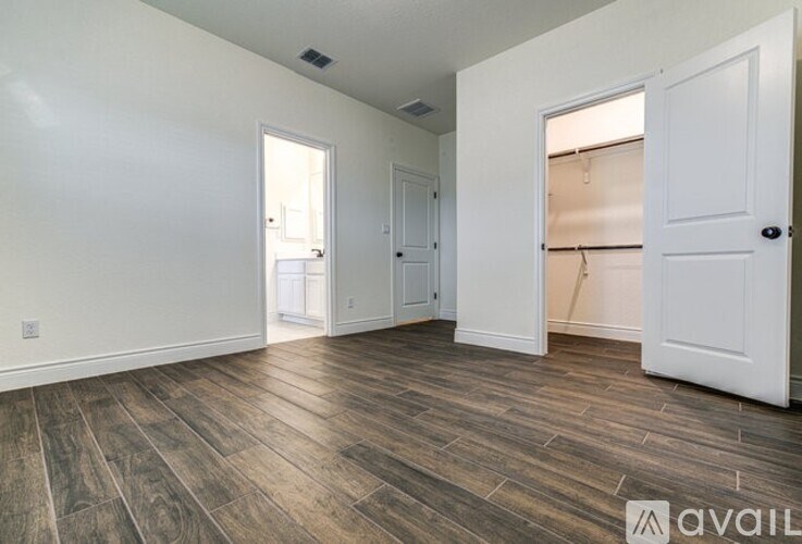A room with white walls and wooden flooring, with two doors and one window.