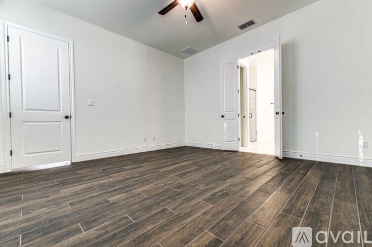 A room with wooden flooring and white walls, with a door on the left and an open door on the right.
