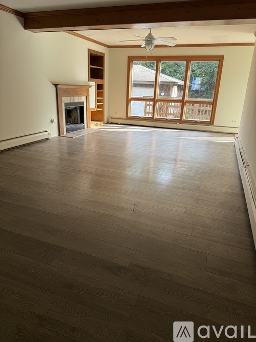 A spacious room with wooden flooring and a fireplace.