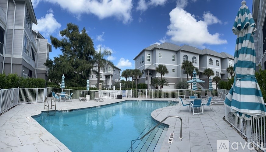 A swimming pool surrounded by a white fence and blue and white striped umbrella.