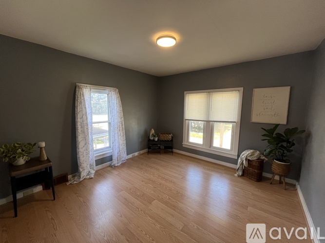 A room with wooden floors and two windows with curtains.