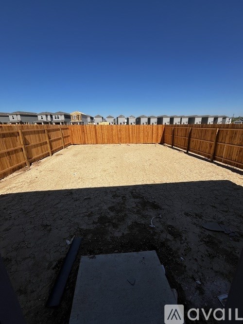 A backyard with a wooden fence and a sandy area in the foreground.