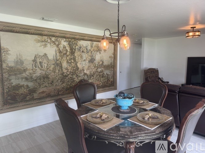 A dining room with a table set for two and a large tapestry hanging on the wall.